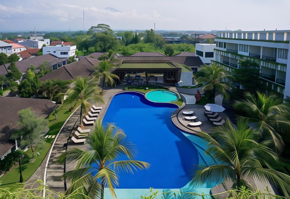 a large outdoor pool surrounded by palm trees , with lounge chairs and umbrellas placed around it at Java Heritage Hotel Purwokerto