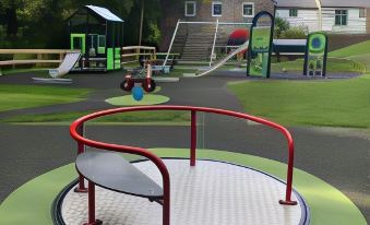a playground with various play equipment , including swings and slides , in a park setting near houses at Trail Lodge