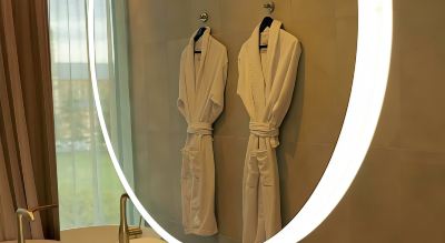 two white bathrobes hanging on a hanger in a bathroom with a window and a door at Oval Hotel at Adelaide Oval, an EVT hotel