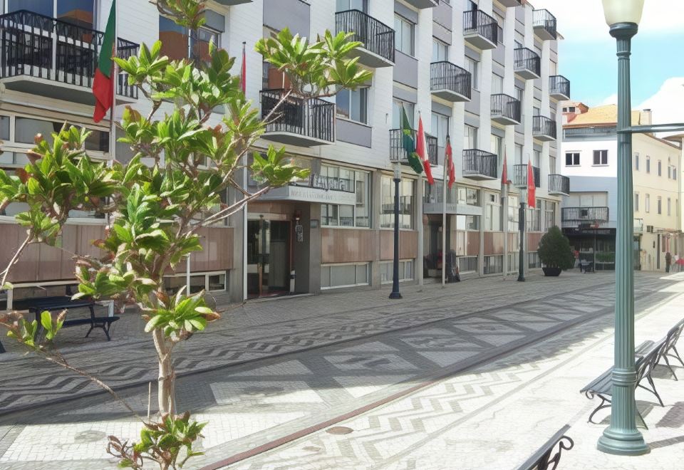 a building with balconies and flags on it , surrounded by trees and a sidewalk with benches at Hotel Imperial