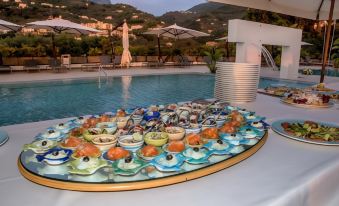 a table with a circular base holds an assortment of food and drinks near a pool at Grand Hotel Moon Valley