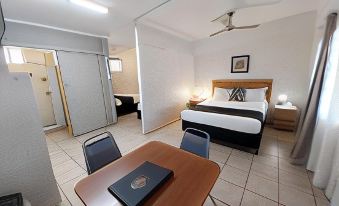 a hotel room with a bed , desk , and chairs is shown from the perspective of someone standing near it at Tropic Coast Motel