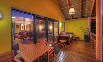 a modern , minimalist bedroom with wooden flooring and large windows , featuring a bed , dining table , and outdoor furniture at Maleny Tropical Retreat