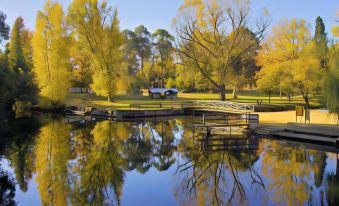 a serene landscape of a park with trees , water , and a wooden walkway , reflecting the autumn colors in the reflection at Abby's Cottages