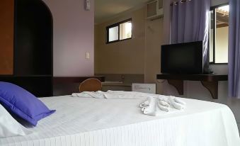 a bed with white sheets and towels is in a room with purple curtains and a television at Hotel del Sol