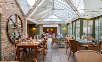 an empty dining room with wooden tables and chairs , under a glass ceiling , under the sky at The Barnsdale