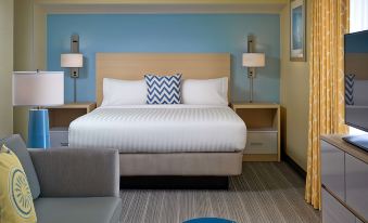 a modern bedroom with a large bed , white linens , and blue walls , accompanied by two lamps and a couch at Sonesta ES Suites Providence - Airport