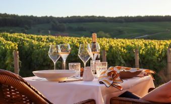 a dining table set for a romantic dinner with wine glasses , plates , and a view of a vineyard at Chateau de Sacy
