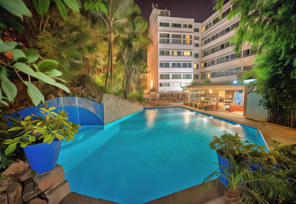 a large outdoor swimming pool surrounded by trees , with a building in the background and a fountain nearby at Marina Bay City Center