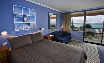 a bedroom with a bed , couch , and window view of the ocean , all set against a blue wall at Swansea Motor Inn Tasmania