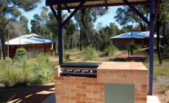 a brick barbecue grill is situated under a wooden structure with blue roofs in a wooded area at Chalets on Stoneville