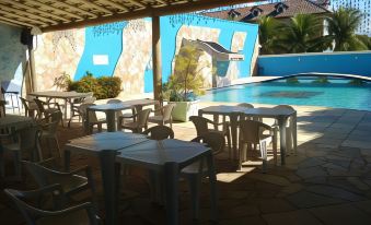 a poolside restaurant with white tables and chairs , a pool in the background , and a mural on the wall at Hotel del Sol