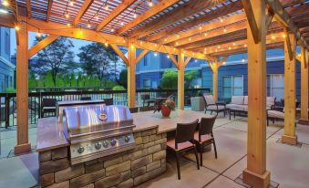 an outdoor dining area with a grill , chairs , and tables under a wooden pergola , surrounded by a garden at Homewood Suites by Hilton Dayton - South/Dayton Mall