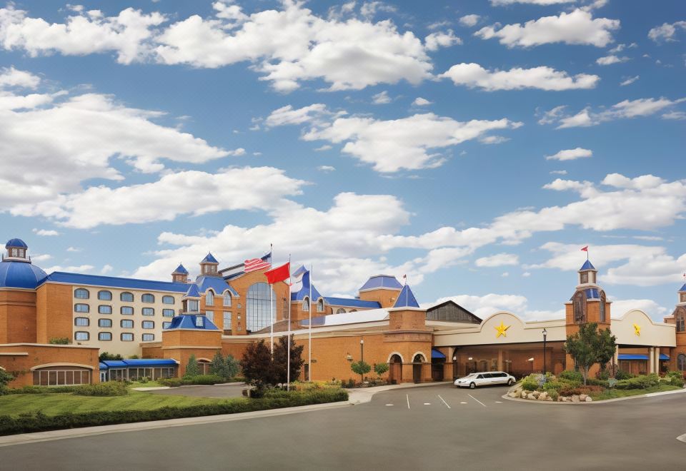 a large hotel with a red roof and blue accents , surrounded by cars and flags , under a blue sky with clouds at Ameristar Casino Hotel Council Bluffs