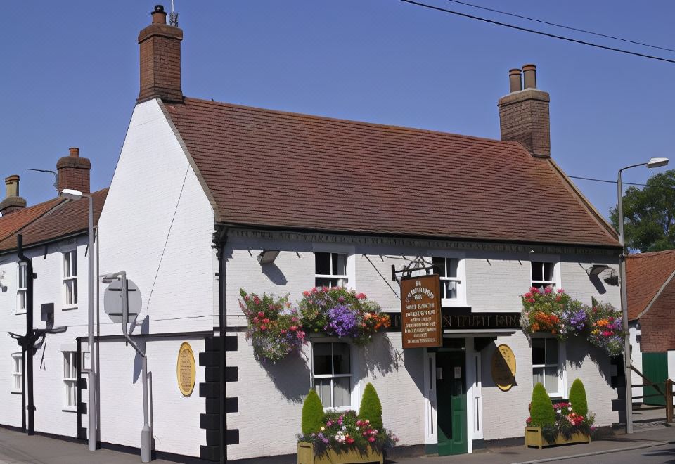 a white building with red - tiled roofs and green shutters , adorned with potted plants and flowers , situated on a street corner at Thornton Hunt Inn