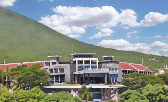 a large building with a red roof is surrounded by trees and mountains , with a blue sky in the background at Sahid Bela Ternate