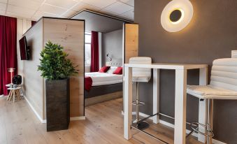 a modern bedroom with a wooden floor , gray walls , and a red accent wall , featuring a bed , desk , and nightstand at Quality Hotel Grand Kongsberg