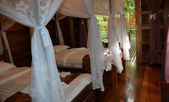 a bed with white drapes is seen in a room with wooden floors and furniture at Borneo Natural Sukau Bilit Resort