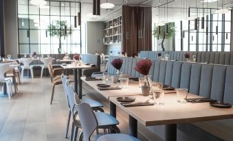 a modern restaurant with multiple dining tables , chairs , and potted plants , set for a large group of people at Hotel Odeon