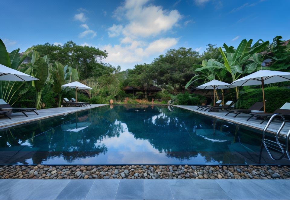 a large , rectangular pool surrounded by lush greenery and trees , with several lounge chairs placed around it at Tam Coc Garden Resort