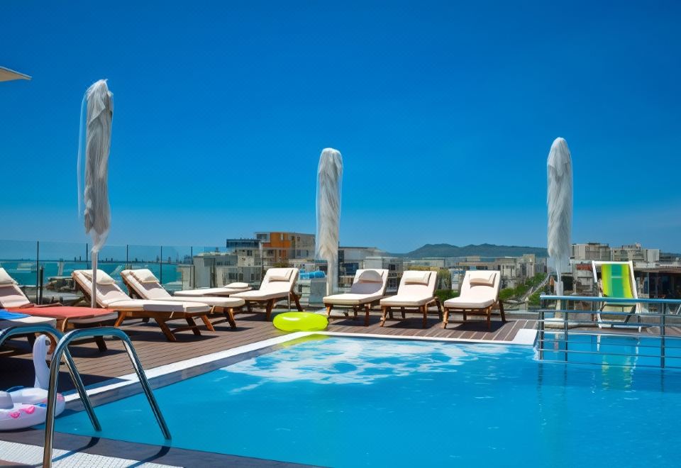 a swimming pool surrounded by lounge chairs and umbrellas , with a view of the ocean in the background at Hotel Empire Albania