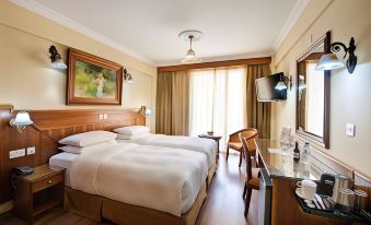 a hotel room with two beds , a window , and a desk , giving a cozy and comfortable atmosphere at Semeli Hotel