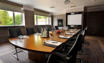 a conference room with a wooden table , chairs , and a large screen on the wall at Macdonald Berystede Hotel and Spa