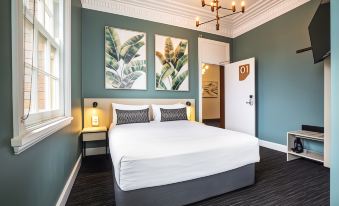 a modern bedroom with blue walls , white bed , and two large paintings on the wall at Nightcap at Pymble Hotel