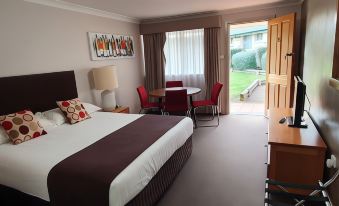 a hotel room with a king - sized bed , a television , and a door leading to a patio at The Aston Motel Tamworth