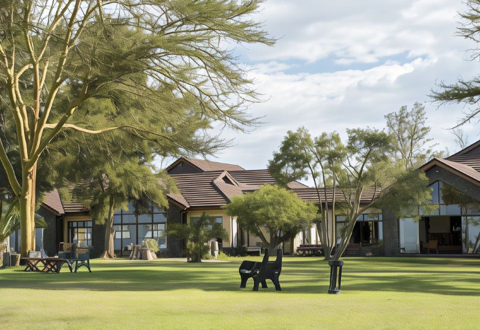 a large house surrounded by a grassy field , with several trees in the background for landscaping at Sweetwaters Serena Camp