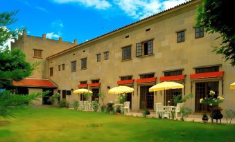 a large stone building with yellow awnings and umbrellas , surrounded by green grass and trees at Parador de Verin