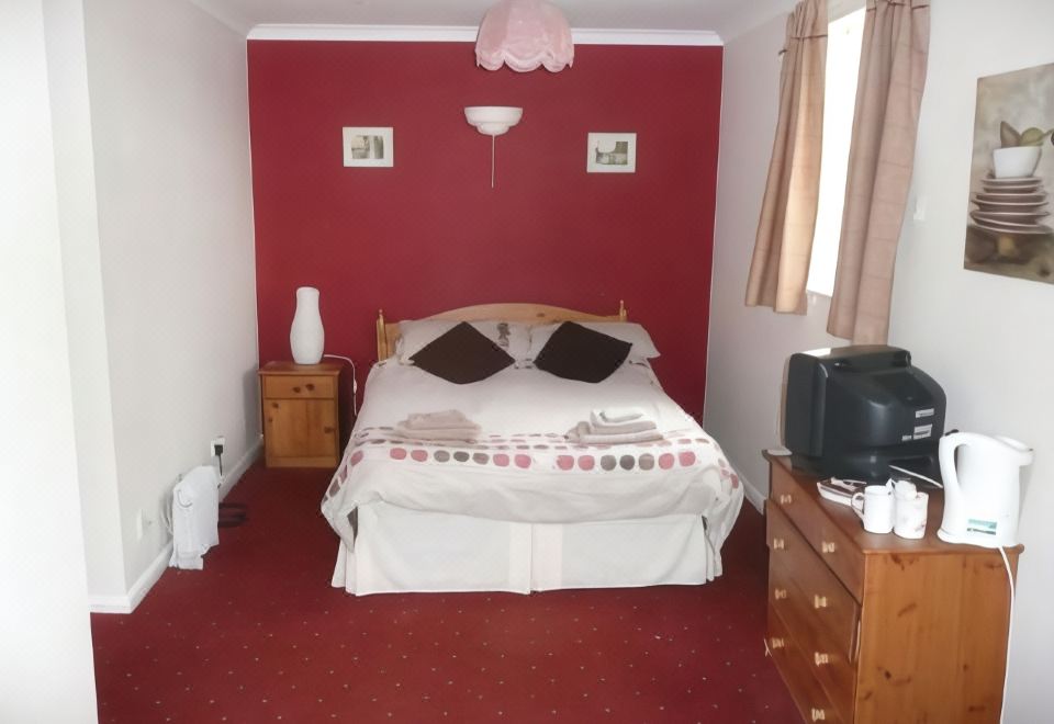 a bedroom with a red wall , a white bed , and a tv in the corner at The Dog Inn