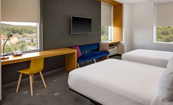 a modern hotel room with a white bed , blue sofa , wooden desk , and large window at Aloft Chapel Hill