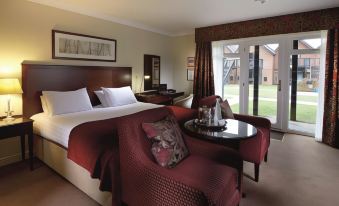 a hotel room with a king - sized bed , a red couch , and a window overlooking a grassy field at Macdonald Elmers Court Hotel and Resort