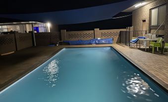 a swimming pool is lit up at night , with a blue canopy and blue lounge chairs at Charlton Motel