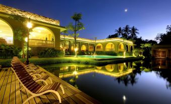 a luxurious hotel with a swimming pool , surrounded by palm trees and lit up at night at The Westlake Hotel & Resort Yogyakarta