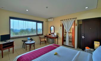 a hotel room with a large bed , desk , and window , along with a view of the ocean at The Jayakarta Suites Komodo Flores