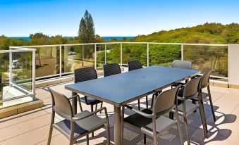 a table and chairs are set up on a balcony overlooking the ocean , with trees in the background at Sand Dunes Resort