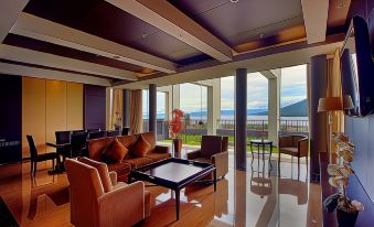 a spacious living room with a view of the ocean , featuring brown couches , chairs , and a dining table at Sahid Bela Ternate