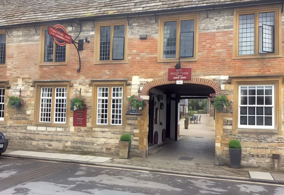 a brick building with a red sign above the entrance , and several potted plants placed outside at The New Inn