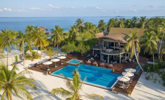 a resort with a pool surrounded by palm trees and overlooking the ocean , creating a serene atmosphere at Outrigger Maldives Maafushivaru Resort