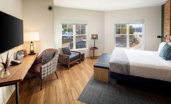 a cozy hotel room with wooden floors , white walls , and large windows , featuring a bed , two chairs , nightstands , lamps , and at Saranac Waterfront Lodge, Trademark Collection by Wyndham