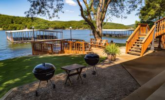 a serene outdoor setting with two charcoal grills , surrounded by trees and a wooden deck , near a river at Point View Resort