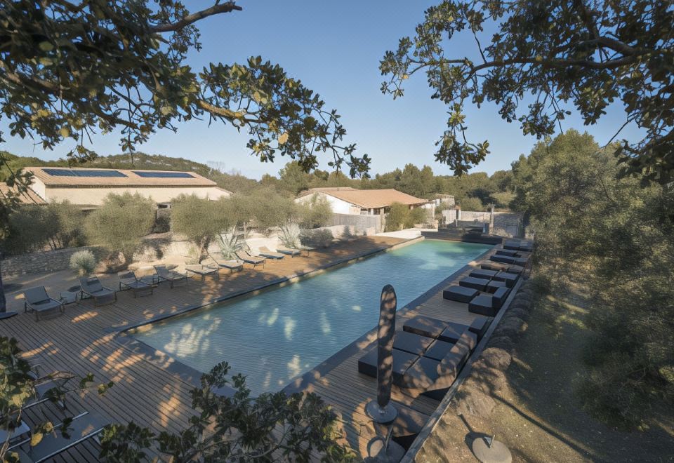 a large outdoor pool surrounded by lounge chairs and umbrellas , with trees in the background at Domaine la Pierre Blanche