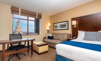 a hotel room with a bed , couch , and desk , along with a view of the city outside the window at New Haven Hotel