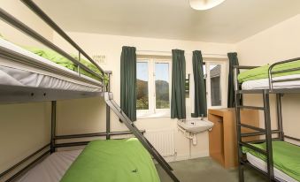 a bunk bed with a green comforter is situated next to a window in a room at YHA Eskdale