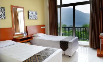 a hotel room with two beds , a window offering a view of the mountains , and a desk with a lamp at Seulawah Grand View