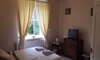 a cozy bedroom with a large window , curtains , and a bed , as well as a television on a wooden table at The Punchbowl Inn