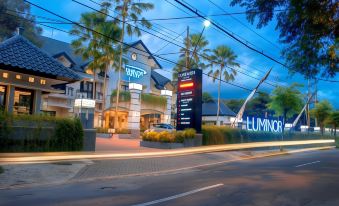 a hotel building with palm trees in front of it and a street lamp in the foreground at Luminor Hotel Jember by WH