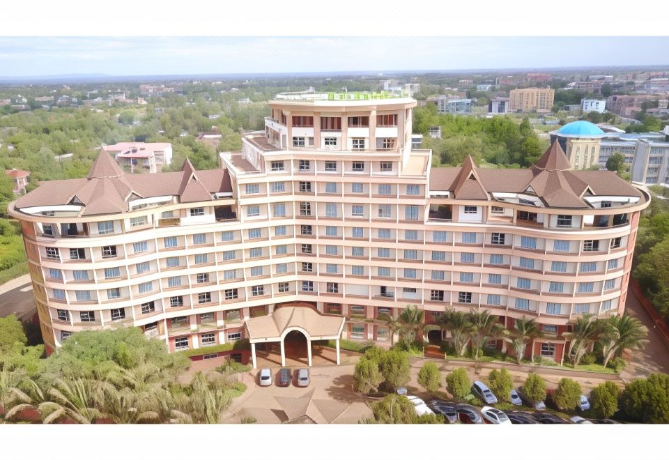a large , multi - story hotel with a green roof and many balconies is surrounded by trees and parking lots at Rainbow Ruiru Resort